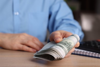 Photo of Money exchange. Woman holding dollar banknotes at wooden table, closeup