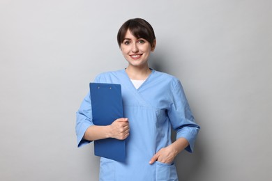 Photo of Portrait of smiling medical assistant with clipboard on grey background