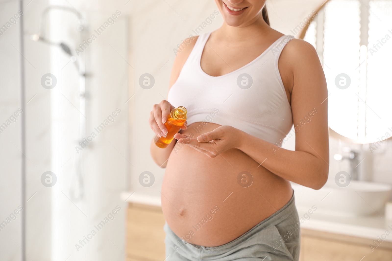 Photo of Young pregnant woman with cosmetic product in bathroom, closeup. Space for text