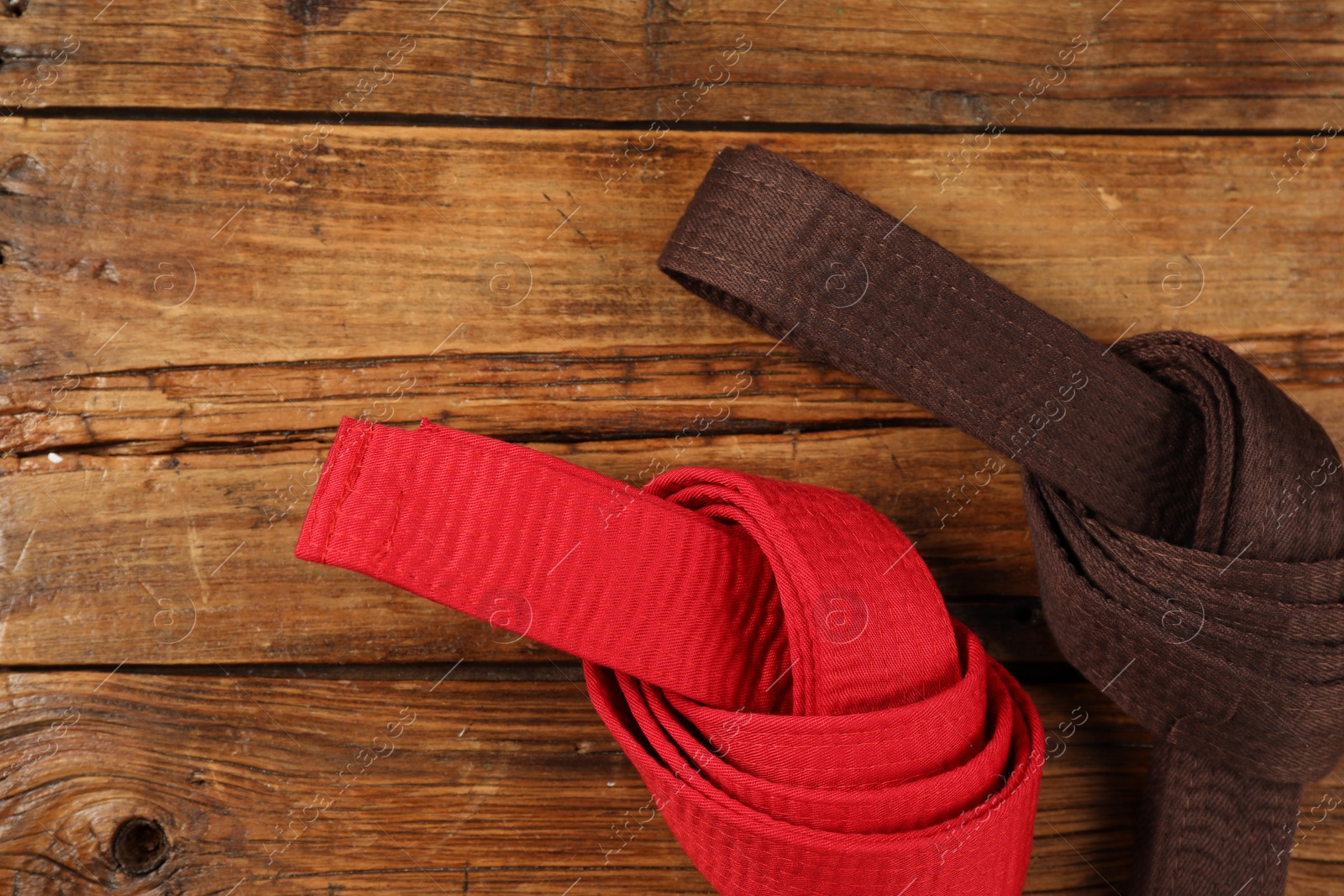 Photo of Red and brown karate belts on wooden background, flat lay