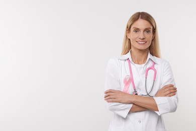 Photo of Doctor with pink ribbon and stethoscope on white background, space for text. Breast cancer awareness
