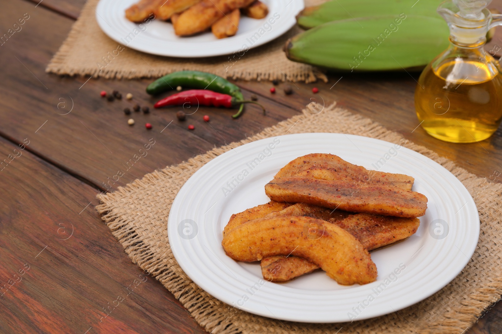 Photo of Delicious fried bananas, cooking oil and different peppers on wooden table