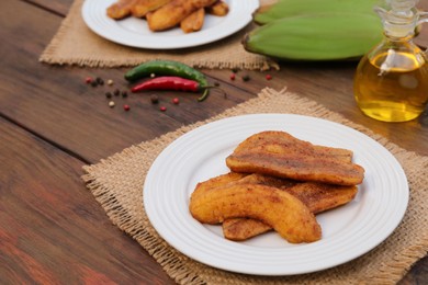 Photo of Delicious fried bananas, cooking oil and different peppers on wooden table