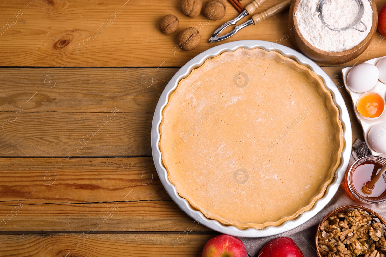 Photo of Raw dough and traditional English apple pie ingredients on wooden table, flat lay. Space for text