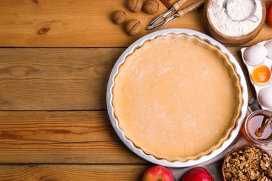 Raw dough and traditional English apple pie ingredients on wooden table, flat lay. Space for text