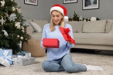Photo of Happy woman in Santa hat opening Christmas gift at home