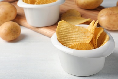 Photo of Bowl of crispy potato chips on white wooden table. Space for text