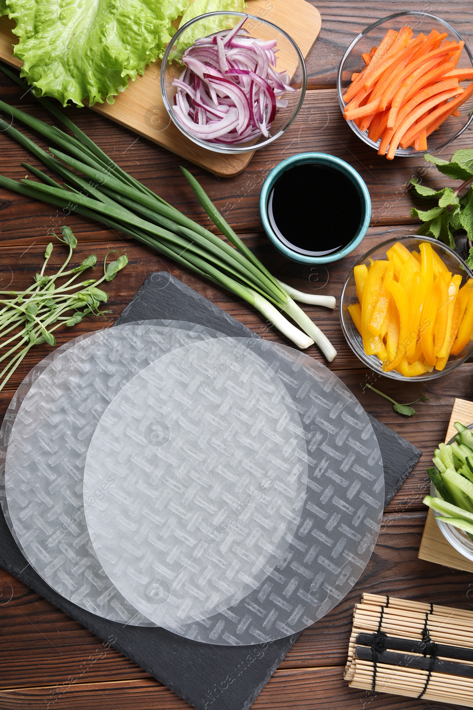 Photo of Rice paper, microgreens and other ingredients for spring rolls on wooden table, flat lay