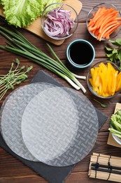 Photo of Rice paper, microgreens and other ingredients for spring rolls on wooden table, flat lay