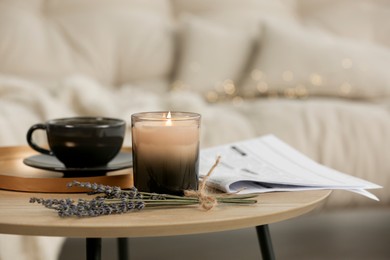 Photo of Beautiful candle, lavender, newspaper and cup on round wooden table in living room