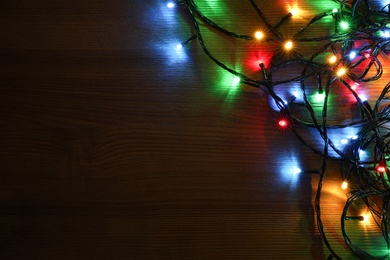 Photo of Colorful Christmas lights on wooden table, top view. Space for text