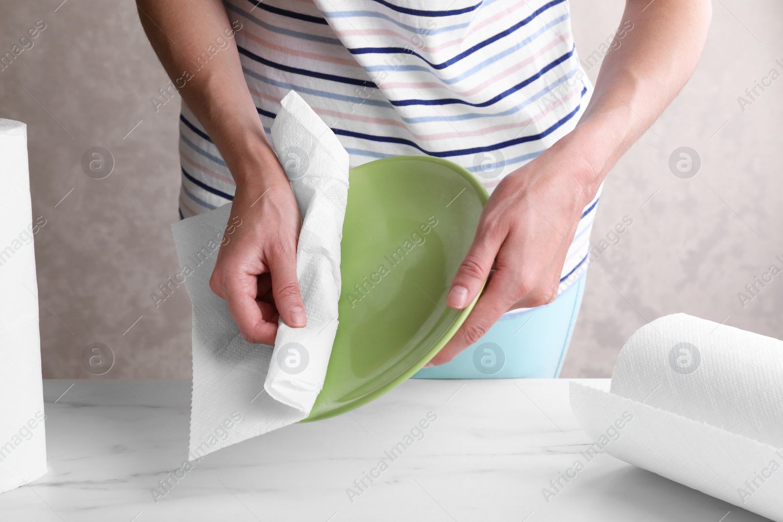 Photo of Woman wiping plate with tissue paper at white marble table, closeup