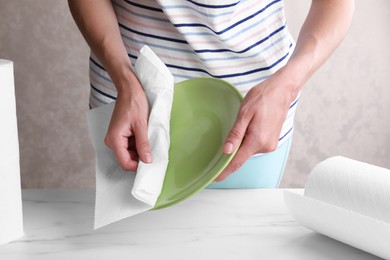 Woman wiping plate with tissue paper at white marble table, closeup