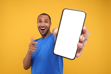 Young man showing smartphone in hand and pointing at it on yellow background