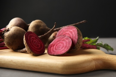 Wooden board with fresh beets on grey table against black background, closeup