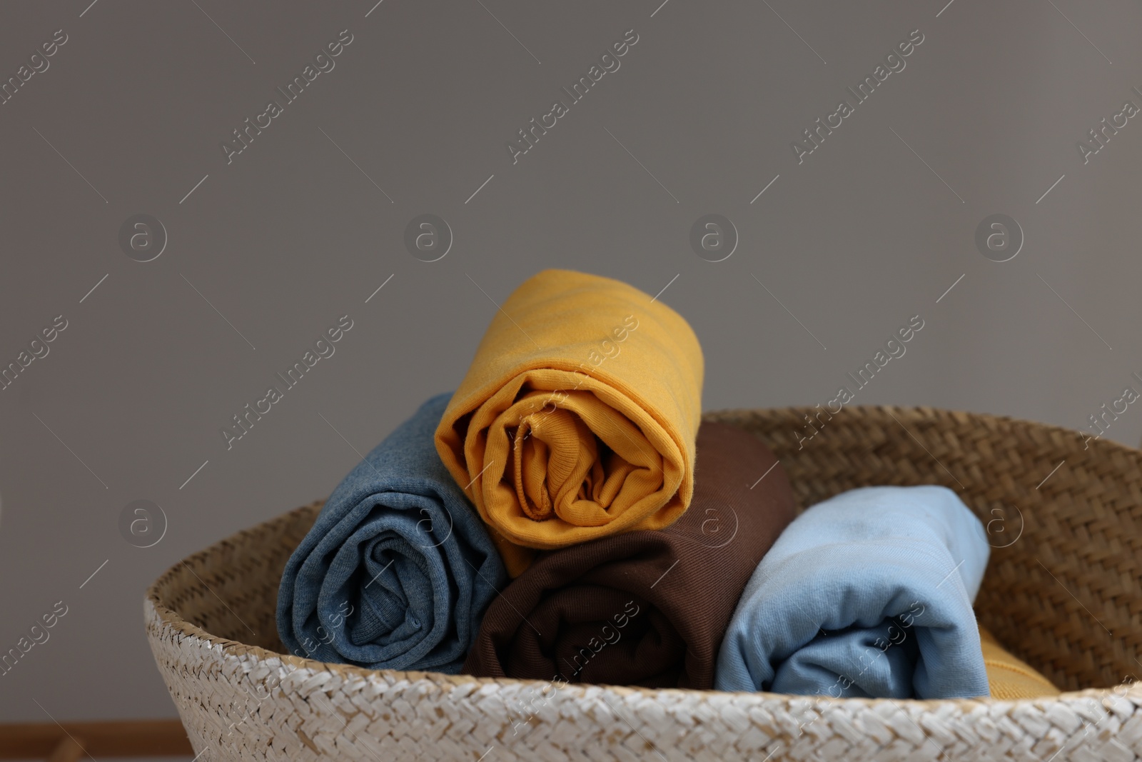 Photo of Different rolled shirts in basket against grey background. Organizing clothes