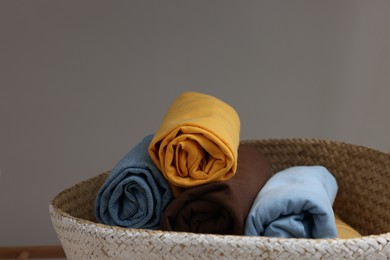 Different rolled shirts in basket against grey background. Organizing clothes