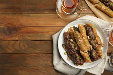 Photo of Delicious sweet baklava with pistachios and hot tea on wooden table, flat lay. Space for text