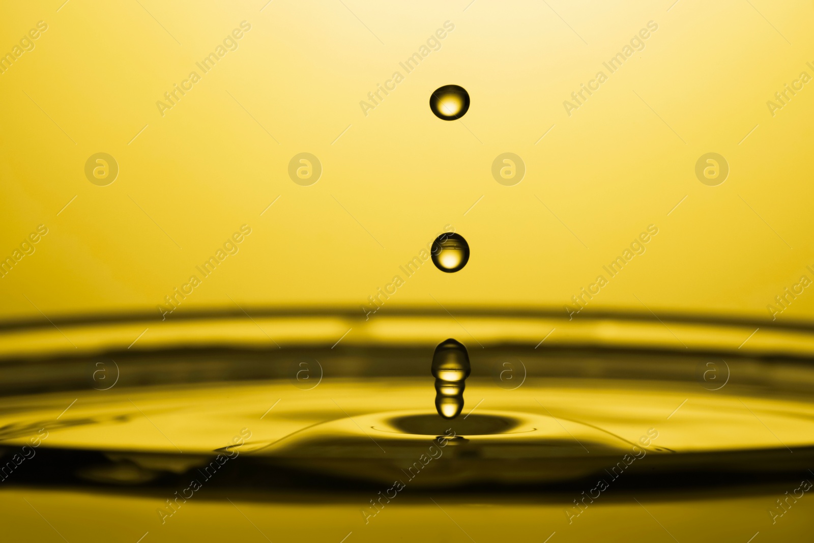 Image of Splash of golden oily liquid with drops on yellow background, closeup