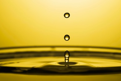 Splash of golden oily liquid with drops on yellow background, closeup