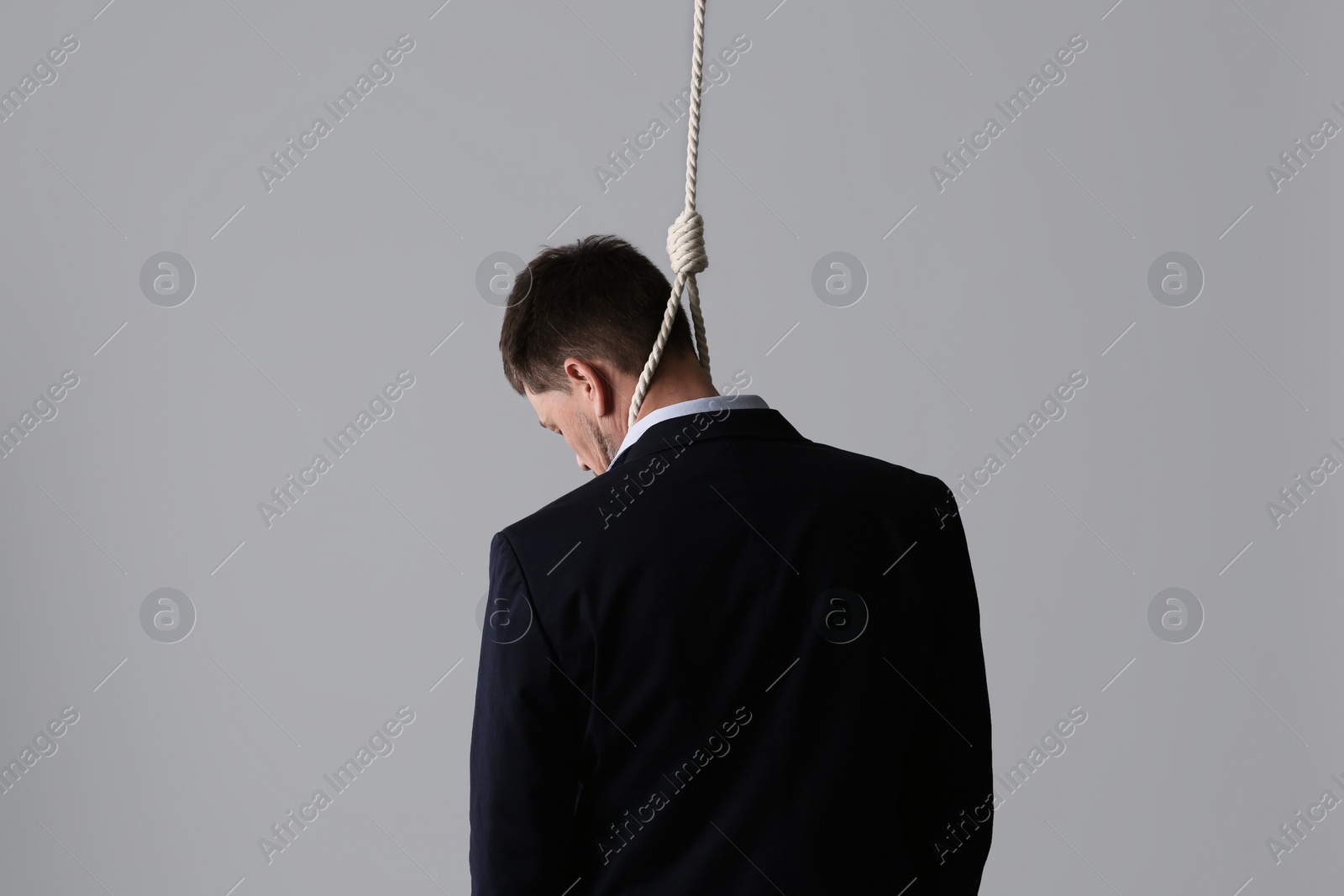 Photo of Businessman with rope noose on neck against light grey background, back view