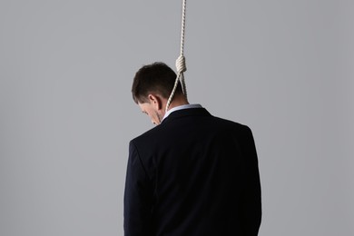 Photo of Businessman with rope noose on neck against light grey background, back view