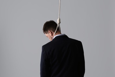 Businessman with rope noose on neck against light grey background, back view