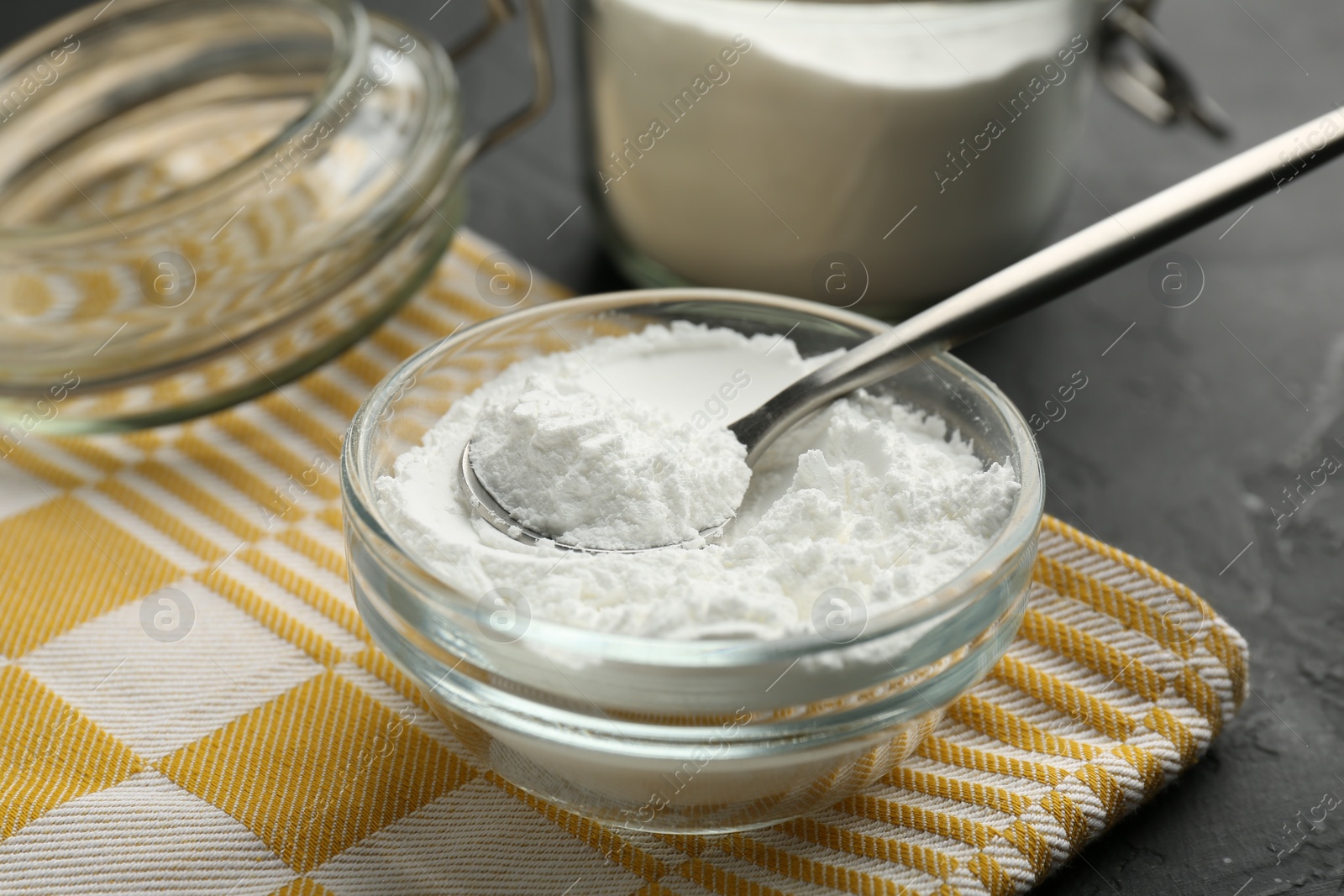 Photo of Baking powder in bowl, jar and spoon on black textured table, closeup