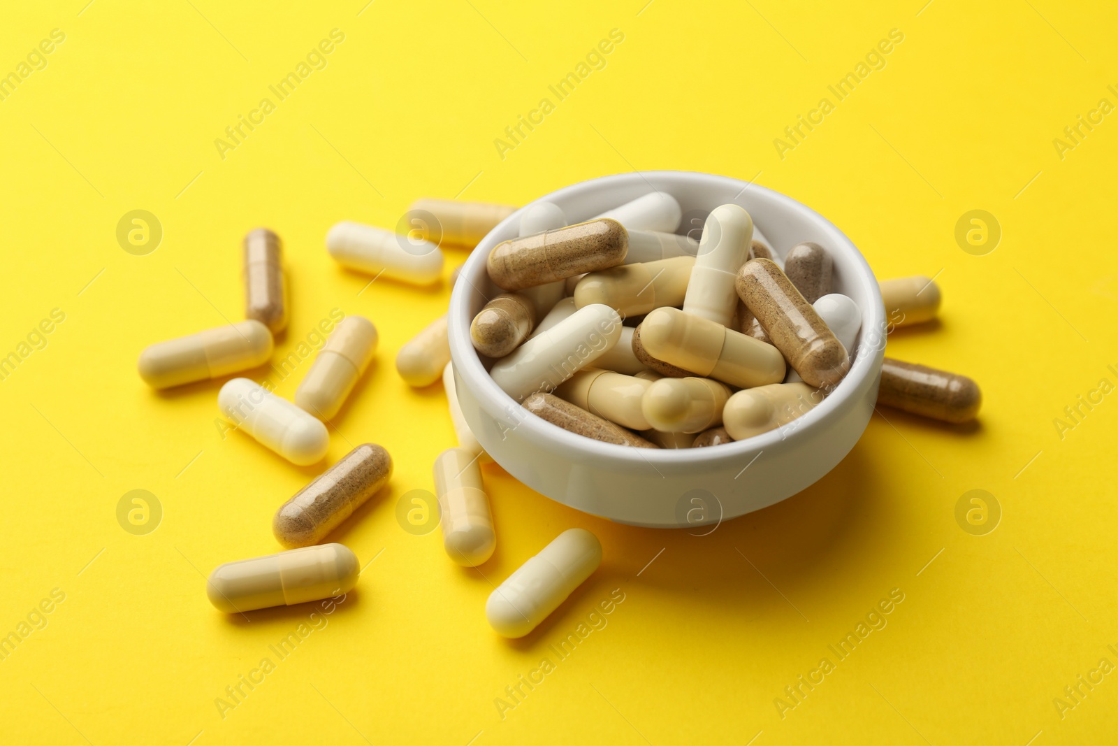 Photo of Different vitamin capsules on yellow background, closeup