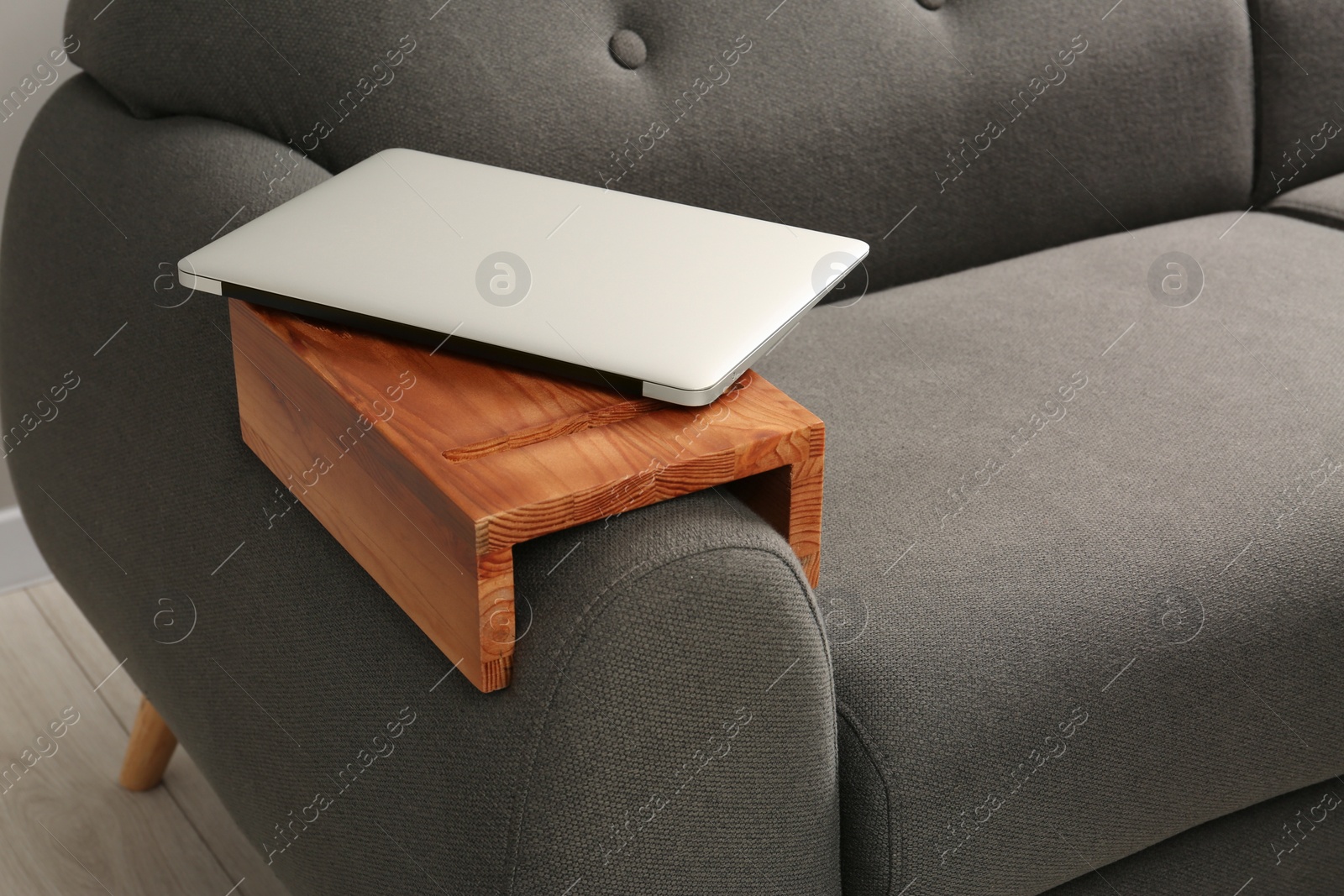 Photo of Laptop on sofa with wooden armrest table in room. Interior element
