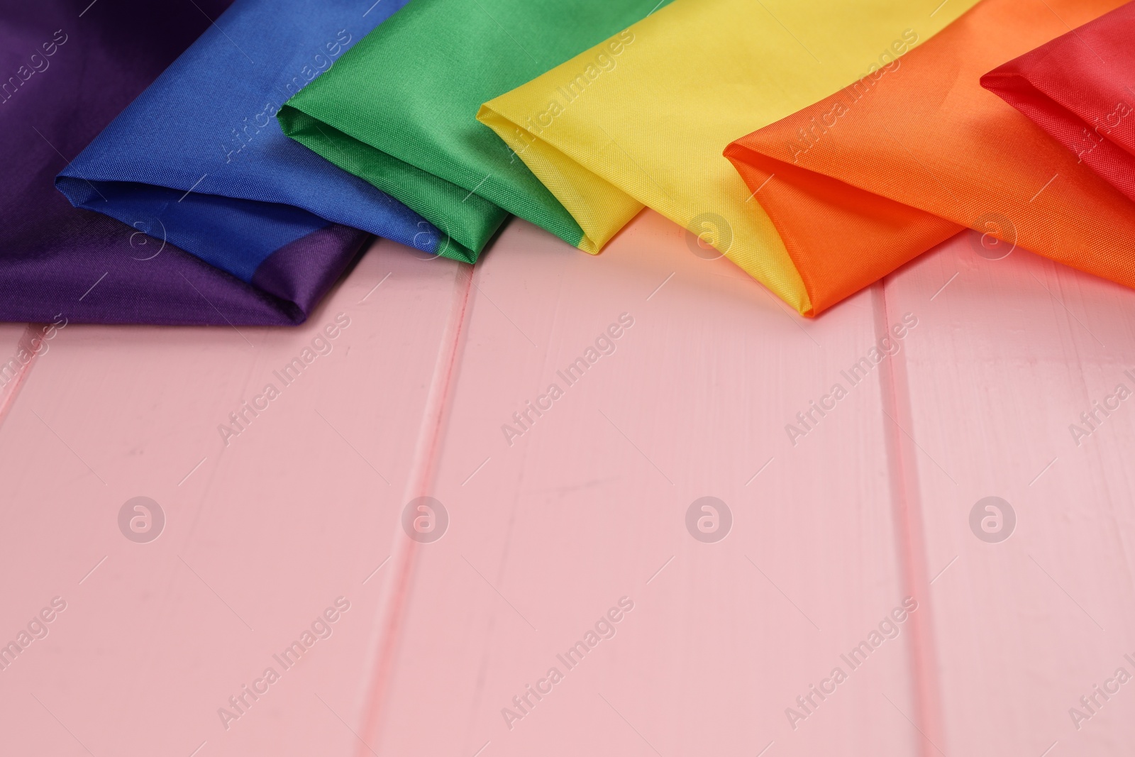 Photo of Rainbow LGBT flag on pink wooden table. Space for text