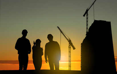 Image of Silhouettes of engineers near construction site at sunrise
