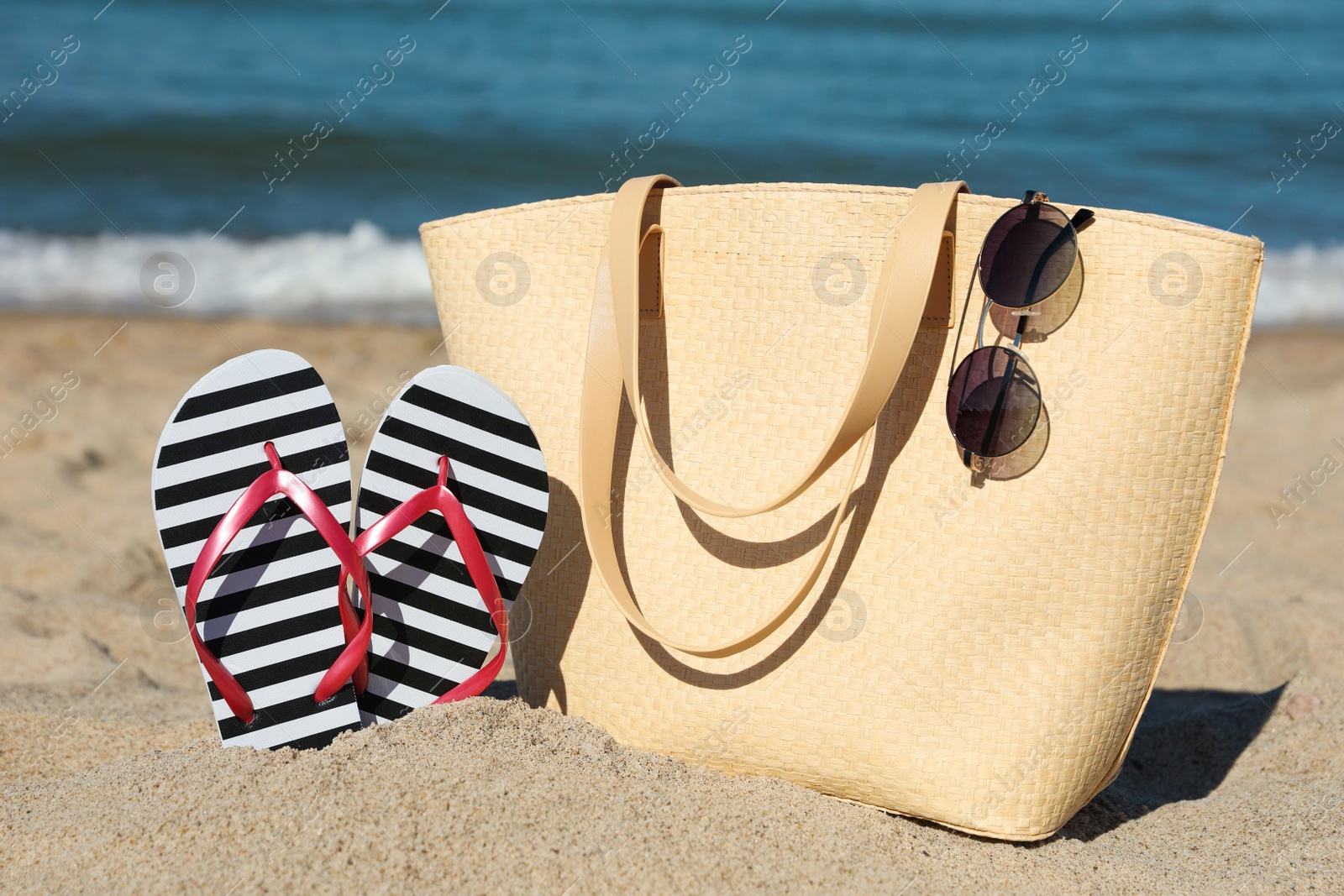 Photo of Striped flip flops, sunglasses and beach bag on sandy seashore