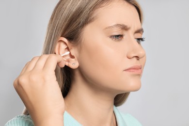 Young woman cleaning ear with cotton swab on light grey background