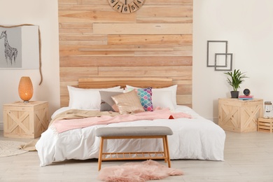 Stylish room interior with comfortable bed near wooden wall