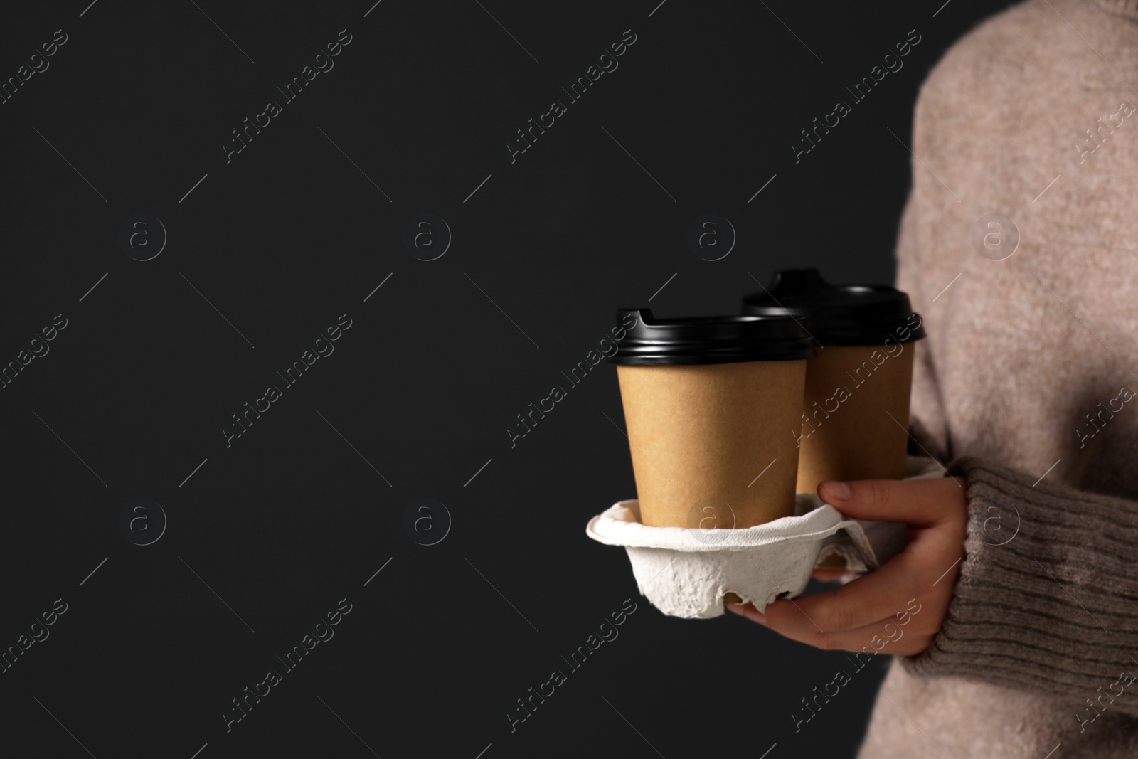Photo of Coffee to go. Woman holding takeaway cardboard cups on black background, closeup. Space for text