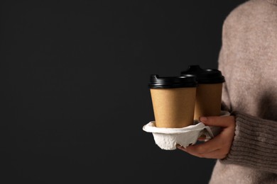 Coffee to go. Woman holding takeaway cardboard cups on black background, closeup. Space for text