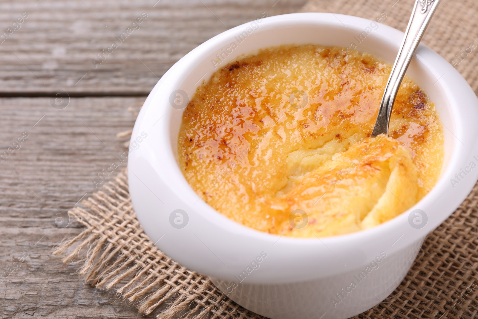 Photo of Delicious creme brulee in bowl served on wooden table, closeup