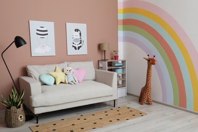 Photo of Cute child's room interior with sofa, toys and rainbow art on wall