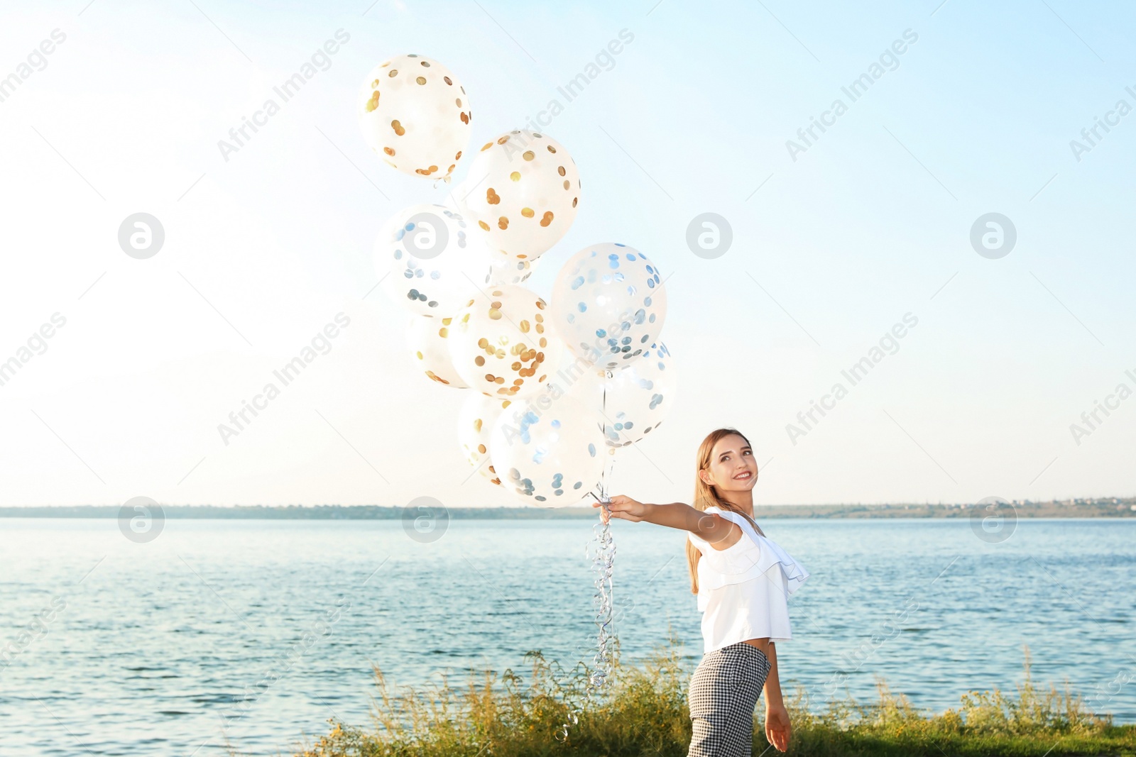 Photo of Beautiful teenage girl holding glitter balloons on riverside