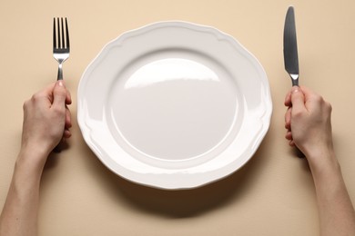 Photo of Woman with cutlery and empty plate at beige table, closeup