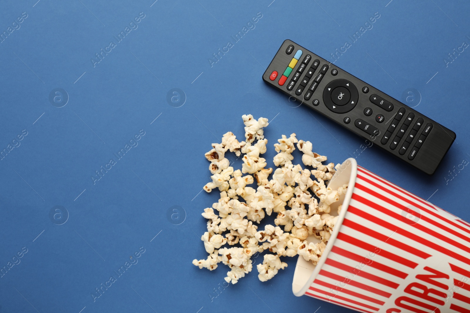 Photo of Remote control and cup of popcorn on blue background, flat lay. Space for text