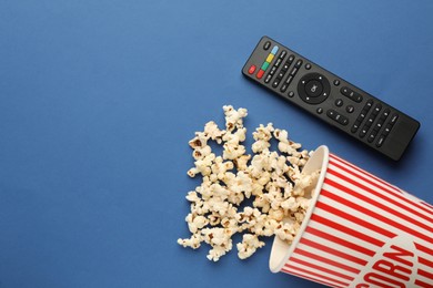 Photo of Remote control and cup of popcorn on blue background, flat lay. Space for text