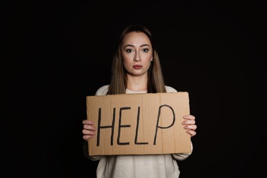 Photo of Unhappy young woman with HELP sign on dark background