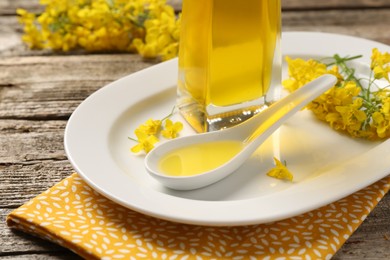 Photo of Rapeseed oil in gravy boat, bottle and beautiful yellow flowers on wooden table, closeup