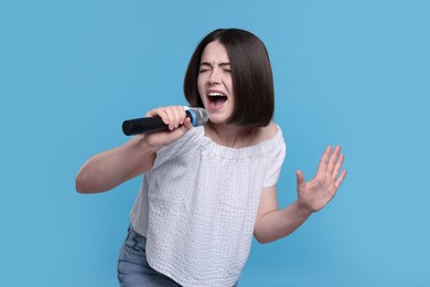 Photo of Beautiful young woman with microphone singing on light blue background