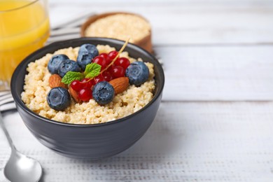 Bowl of delicious cooked quinoa with almonds, cranberries and blueberries on white wooden table, space for text