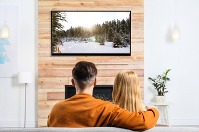 Couple watching TV on sofa in living room with decorative fireplace