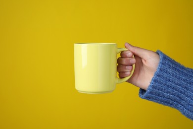 Photo of Woman holding porcelain mug on yellow background, closeup. Space for text