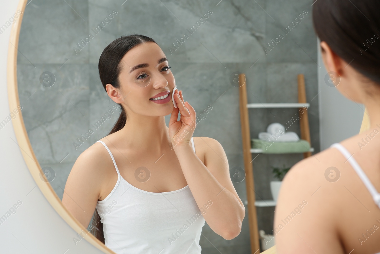 Photo of Beautiful woman removing makeup with cotton pad near mirror indoors